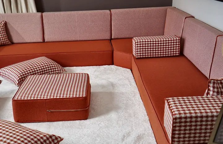 Terracotta linen L-shaped floor couch with blush backrests, gingham pillows and an ottoman on a white rug
