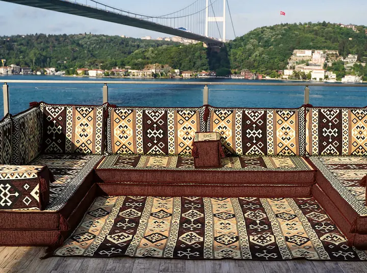 Thick brown and cream kilim-pattern U-shaped majlis seating arranged around a matching rug on an open wooden deck