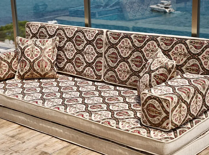 Single floor sofa in a brown, cream and red tulip ogee weave with box bolsters and a pillow on a wooden terrace above the water