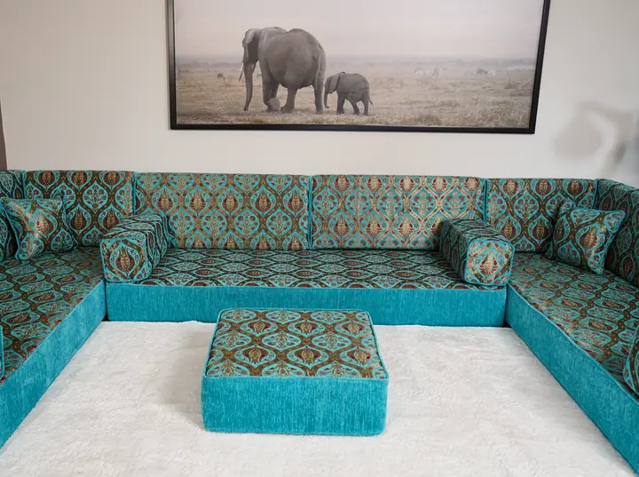 Turquoise and brown patterned floor sofa lining three walls around a white rug, with a turquoise ottoman in the middle of the room
