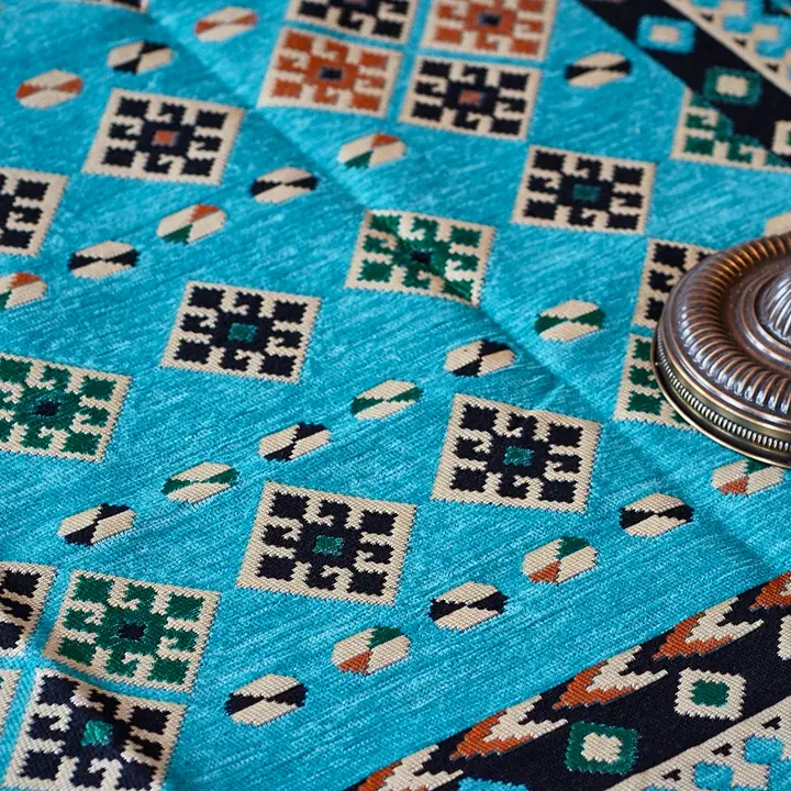 Turquoise flat-weave close-up with orange and black geometric motifs and the base of a floor lamp at one side