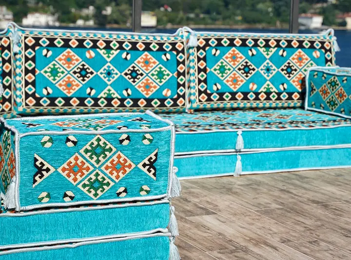 Close angled view of a turquoise kilim floor sofa built on two stacked seat layers, with a cube armrest at the end