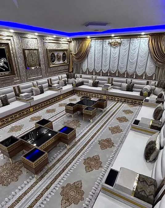 Side view of white and gold seating under a blue ceiling glow, with framed wall art and nesting tables with dark tops